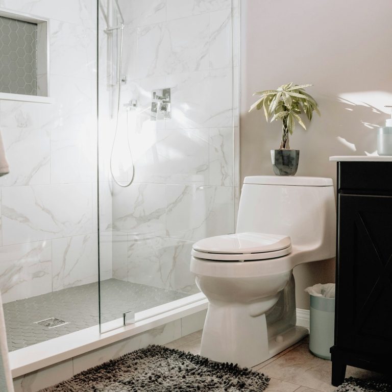 Modern bathroom remodel with glass walk-in shower, marble-look tile, toilet and dark vanity